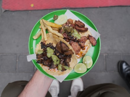 A colorful plate of assorted grilled meats, fries, lime wedges, and dipping sauces on a green plate held by a person. End.