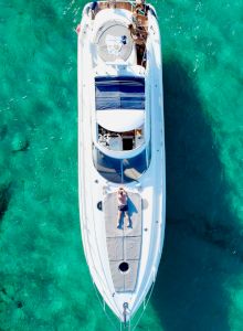 A white motorboat on clear turquoise water, seen from above with people on board, sunny day, sea green shadows.