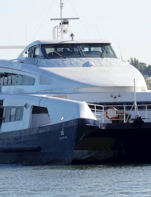 A two-story white and blue luxury yacht cruising on calm water, with a sleek silhouette and open deck stairs, scenic coastline in background.